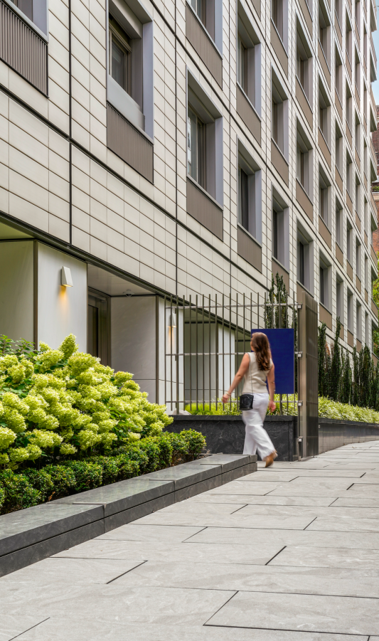 A city sidewalk with greenery and a building to the left