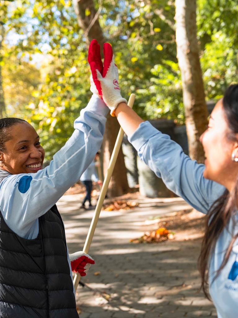 2 people hi fiving in a park while cleaning