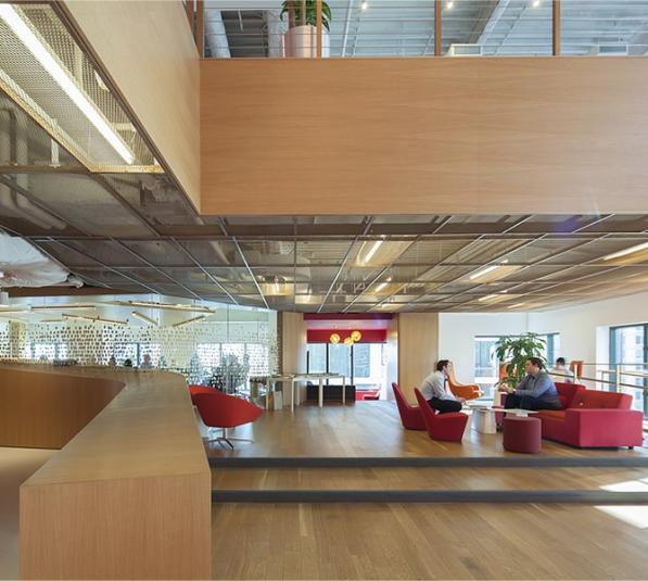 A large open office space with sitting areas and a glass wall meeting room
