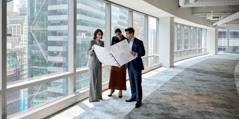 3 people standing in a hallway looking at building plans