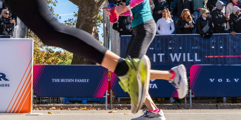Marathon runners passing in front of Rudin signage  