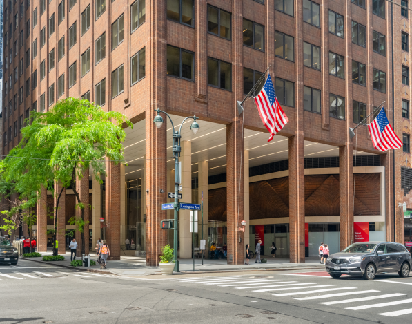 A Street view of the corner of 560 Lexington Avenue with American flags on one side and trees on the other.