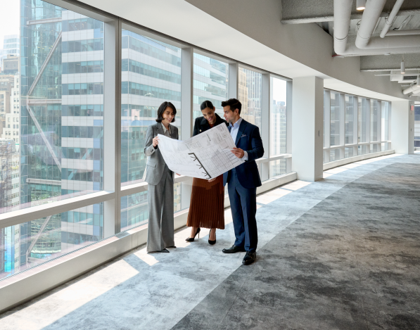 Three professionals in a tall office building reviewing a document next to windows