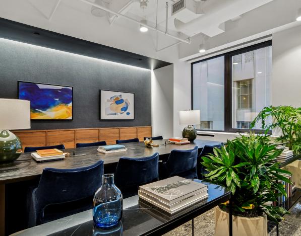 A meeting room in the Industrious office with lamps on a long table with blue chairs placed around it