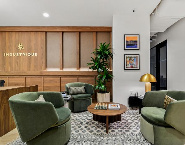 The reception area of Industrious' office with green chairs around a coffee table