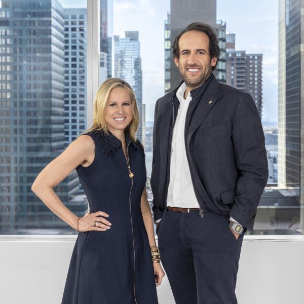 The Rudin Executive Team stands in front of a window with a city scape in the background