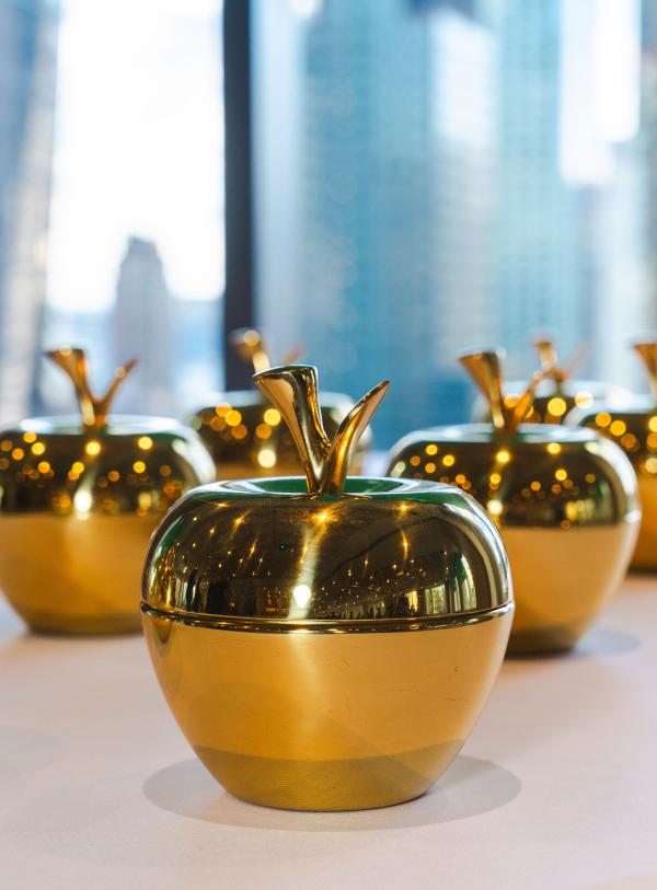 Golden apples sit on a white table with a city view in the background